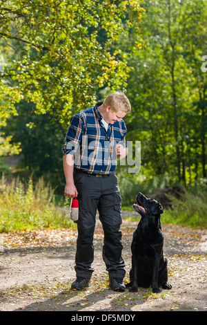 Hundebesitzer schult seine Labrador Retriever auf outdoor, Hund sitzt auf, neben, Hochformat Stockfoto