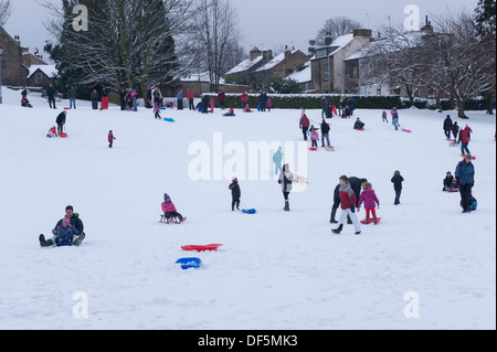 Viele Personen (Erwachsene und Kinder) mit Spaß für die ganze Familie im Winter Schnee, Rodeln, Down Hill in Parkstellung - Riverside Gardens Ilkley, Yorkshire, England, UK. Stockfoto