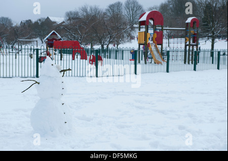 Kalte Winter Szene mit solitären Schneemann stehend durch einen Kinderspielplatz in frischem Weiß Schnee - Ilkley Park, West Yorkshire, England, UK. Stockfoto