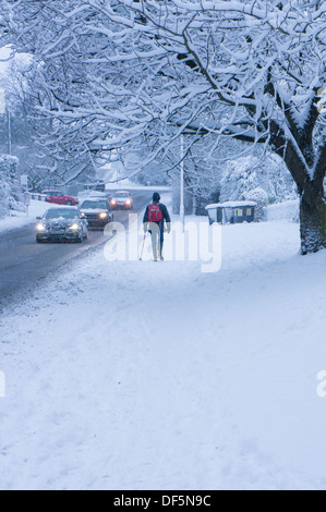 Winter Szene mit schneebedeckten Fahrbedingungen für Autos auf der Straße und einsamen Fußgänger gehen auf schneebedeckte Bürgersteig - guiseley Leeds, West Yorkshire, UK. Stockfoto