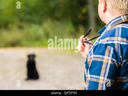 Hundebesitzer schult seine Labrador Retriever mit einem Pfiff, Labrador Retriever sitzt auf Hintergrund Stockfoto