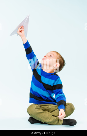 Fröhlicher Junge spielt mit Papierflieger im Studio, hellblauen Hintergrund Stockfoto