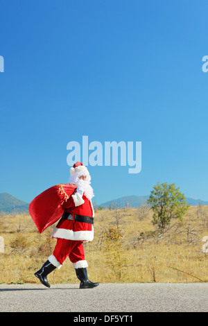 Santa Claus mit Tasche zu Fuß auf einer Landstraße Stockfoto