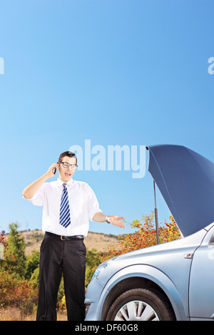 Junger Geschäftsmann stand in der Nähe ein kaputtes Auto und ein telefonieren Stockfoto