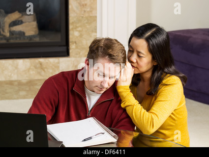 Foto von reifes Paar mit Frau Flüstern ins Ohr des Menschen, während der Arbeit von zu Hause aus Stockfoto