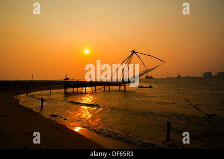 Kochi chinesischen Fischernetzen und das Boot mit den Fischern auf Sonnenuntergang in Kerala. Fort Kochin, Kochi, Süd-Indien Stockfoto