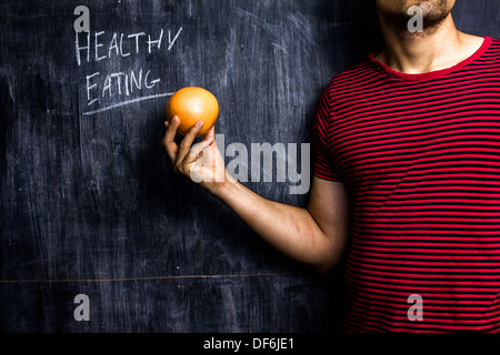 Junger Mann stand vor der Tafel hielt eine Grapefruit mit gesunden Beratung hinter ihm geschrieben Stockfoto