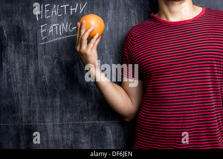 Junger Mann stand vor der Tafel hielt eine Grapefruit mit gesunden Beratung hinter ihm geschrieben Stockfoto