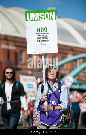 Manchester, UK. 29. September 2013. Eine Frau in den Fünfzigern ein Schild hochhalten und tragen ein Unisono-Lätzchen während einer Nord-West TUC organisiert März und Rallye National Health Service (NHS) Arbeitsplätze und Dienstleistungen von Kürzungen und Privatisierungen verteidigen wollte. Der März fällt mit der konservativen Partei Konferenz 2013 in der Stadt statt. Bildnachweis: Russell Hart/Alamy Live-Nachrichten. Stockfoto