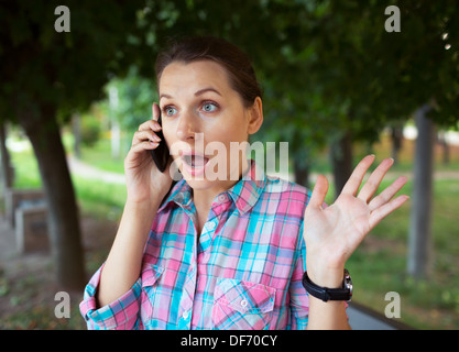 Porträt von überrascht schöne Frau im Park am Telefon sprechen Stockfoto