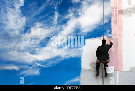 Maler malt strahlend blauen Himmel an der städtischen Wand Stockfoto