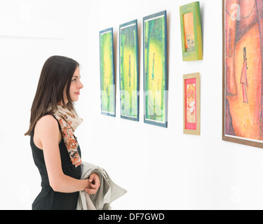 Seitenansicht des jungen kaukasischen Frau stehen in einer Kunstgalerie vor bunten gerahmten Gemälden dargestellt auf einer weißen Wand Stockfoto
