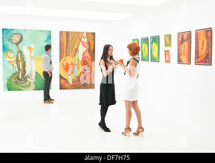 zwei Frauen stehen und einen Drink in einer Kunstgalerie Stockfoto