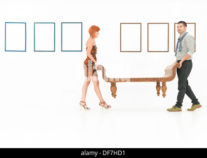 zwei kaukasischen Personen tragen eine Holzbank in einem weißen Raum mit leere Frames angezeigt an Wänden Stockfoto