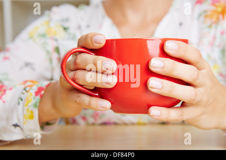 Weibliche Hände halten eine große rote Kaffeetasse Stockfoto