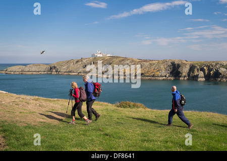 Drei Wanderer zu Fuß auf Küstenweg mit Lynas Point Leuchtturm über Llaneilian Isle of Anglesey North Wales UK Großbritannien Stockfoto