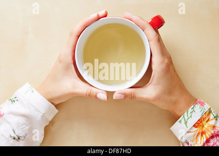 Zwei Hände halten Kamillentee in einer Tasse von oben Stockfoto