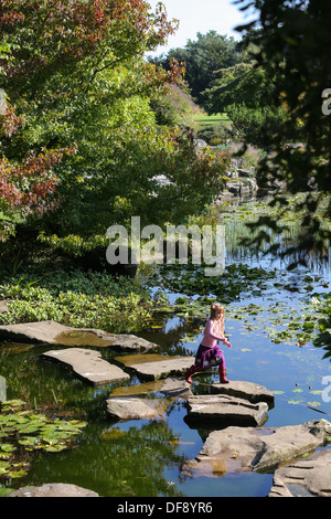 Cambridge University Botanic Garden im frühen Herbst und HER Mädchen geht über SKIPPING STONES durch A Teich. Stockfoto