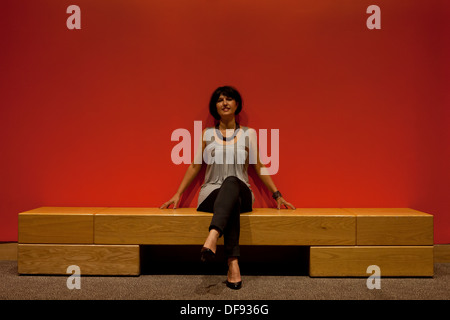 Frau sitzt an einer roten Wand Stockfoto