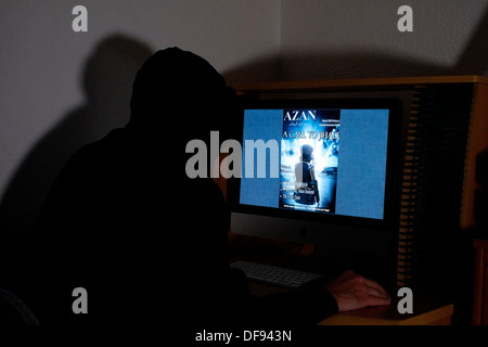 mit Kapuze und maskierten Mann betrachtet die terroristischen Magazin Azan online auf seinem computer Stockfoto