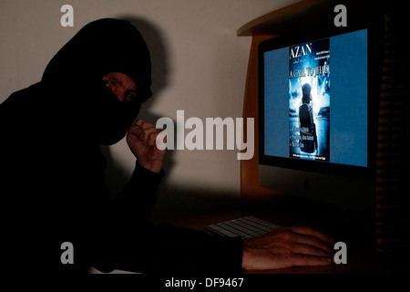 mit Kapuze und maskierten Mann betrachtet die terroristischen Magazin Azan online auf seinem computer Stockfoto