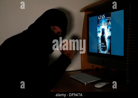 mit Kapuze und maskierten Mann betrachtet die terroristischen Magazin Azan online auf seinem computer Stockfoto