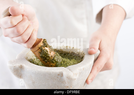 Cooks Hände Schleifen Pesto auf traditionelle Weise, mit einem hölzernen Mörser Stockfoto