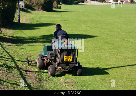 Platzwart Cutting The Grass On A Rasenmäher auf öffentlichen Sportplatz Stockfoto