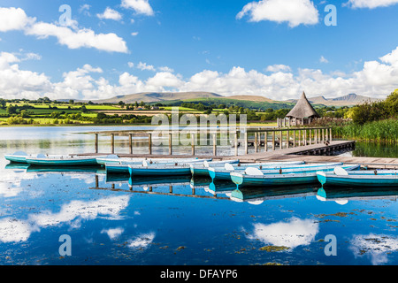 Ruderboote vertäut am Llangors See in den Brecon Beacons National Park, Wales mit Crannog auf der rechten Seite. Stockfoto