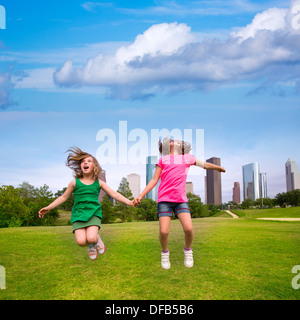 Zwei Schwester Mädchen Freunde springen glücklich halten hand in urbanen moderne Skyline Park Rasen Stockfoto