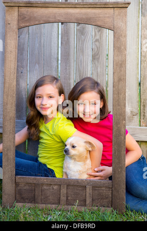 Twin Sisters Portrait mit Chihuahua Hund auf Grunge Holz Rahmen auf Rasen sitzen Stockfoto