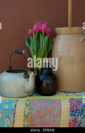 Eine alte Kanne, Krug, Butterfass, rosa Tulpen auf eine bunte handgemachte quilt. Stockfoto