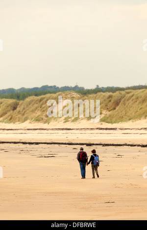 Ein paar Hände halten in der Liebe zu Fuß auf einer menschenleeren Strand von Whitby auf Anglesy mit Sanddünen in den Boden zurück, Anglesey, Wales, Großbritannien Stockfoto