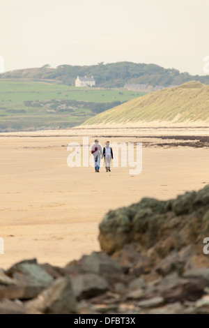 Ein paar Hände halten in der Liebe zu Fuß auf einer menschenleeren Strand von Whitby auf Anglesy mit Sanddünen in den Boden zurück, Anglesey, Wales, Großbritannien Stockfoto