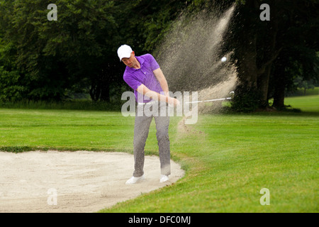 Ein Profi-Golfer schlägt seinen Ball aus einem Bunker mit dem Sand und den Ball in der Luft. Stockfoto