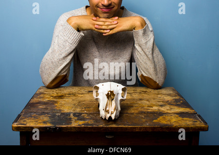 Lächelnd jungen Mann an einem Schreibtisch mit Ziege #s Schädel vor ihm Standortwahl Stockfoto