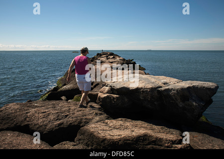 Im Spätsommer geht eine Frau entlang der Mole im Hammonasset Beach State Park, Madison, Connecticut. Stockfoto