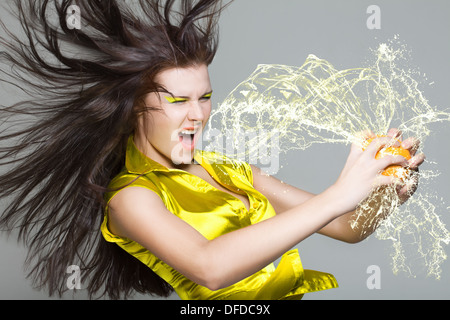 Frau zerkleinert Orangensaft und Sprays kommen ihr ins Gesicht Stockfoto