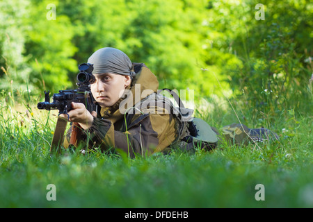 Soldat in Camouflage mit einer Kalaschnikow auf der Wiese liegend Stockfoto