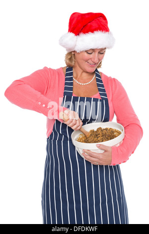 Eine Frau in Weihnachtsmütze hält eine Schüssel und mischen die Zutaten für einen Weihnachtskuchen, isoliert auf einem weißen Hintergrund. Stockfoto