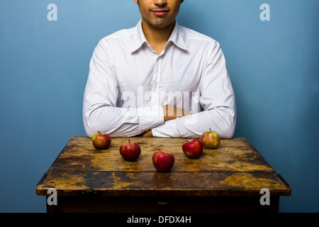 Junger Mann sitzt am Tisch mit fünf Äpfeln Stockfoto