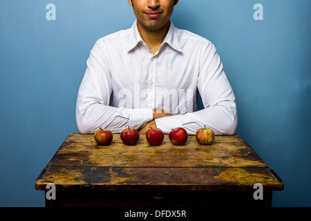 Junger Mann sitzt am Tisch mit fünf Äpfeln Stockfoto