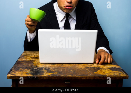 Junge Unternehmer wundert sich über etwas, das er auf seinem Laptop zu sehen ist und fast verschüttet seinen Kaffee drauf Stockfoto