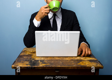 Junger Geschäftsmann ist Kaffee trinken und arbeitet an seinem Laptop an einem alten Schreibtisch Stockfoto