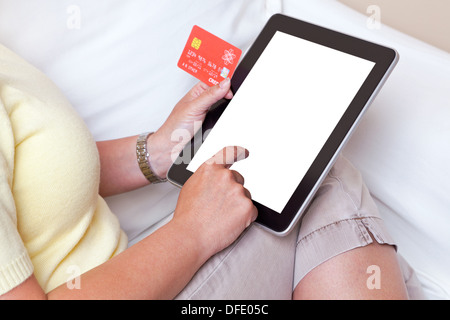 Eine Frau saß zu Hause machen einen Online-Kauf auf ihrem Tablettcomputer, geben Sie ihre Kreditkarten-details Stockfoto