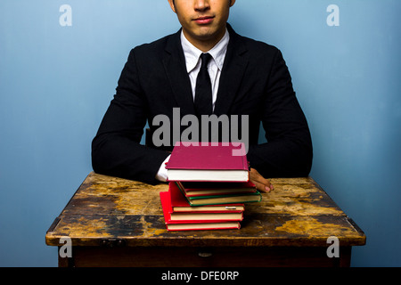 Glückliche junge Unternehmer sitzen an einem alten Schreibtisch mit einem Stapel Bücher Stockfoto