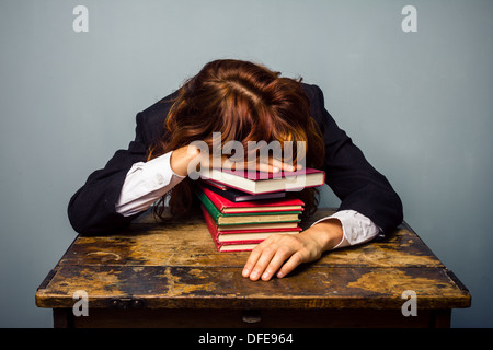 Junge Geschäftsfrau schläft mit dem Kopf ruht auf einem Stapel Bücher vor ihr am Schalter Stockfoto