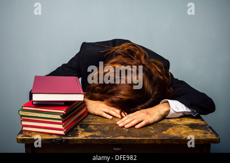 Junge Geschäftsfrau ist am Schreibtisch mit einem Stapel Bücher vor der ihr eingeschlafen Stockfoto