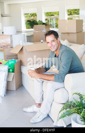 Porträt von lächelnder Mann Kaffeegenuss auf Sofa unter Kartons Stockfoto