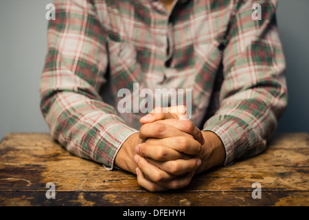 Junger Mann sitzt an alten Holztisch mit seinen Händen gefaltet Stockfoto